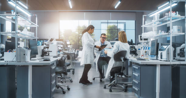 istock Modern Medical Laboratory: Scientists Working Together on a Research Project. Male and Two Young Women Talking About Vaccine Development Methods and Biotechnology Breakthroughs 2190227436
