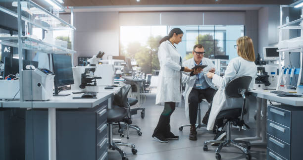 istock Female Research Scientist Having a Conversation with Two Bioengineers About the Effects of Different Pharmaceutical Drugs. Employees Looking at an Online Report in a Modern Science Laboratory 2190227465
