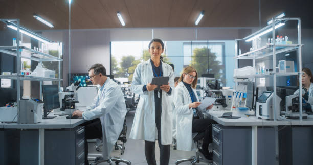 istock Group of Scientists in White Lab Coats Working in a Workplace, Sitting Behind Desks and Using Computers. Young Creative People Working in a Research Laboratory 2190227629