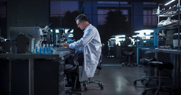 istock Portrait of a Caucasian Scientist Working in a Laboratory in the Evening, Using Advanced Microscope, Writing Down Research Data on a Computer. Biotechnology Specialist Using Modern Equipment 2190228119