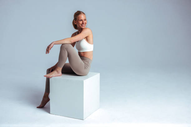istock Smiling sporty woman sitting on white cube in studio 2190228592