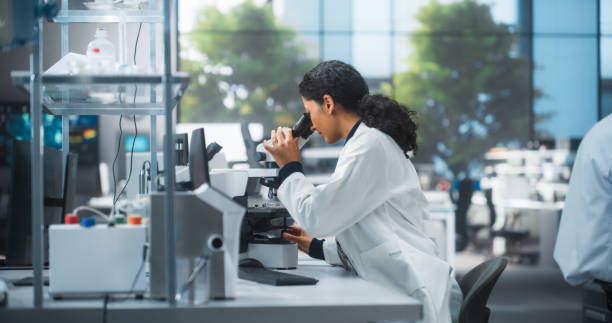 istock Medical Research and Development Laboratory: Beautiful Hispanic Female Scientist Working on a Computer and Looking at a Sample in a Petri Dish Under a Microscope. Advanced Biotechnology Lab 2190228673