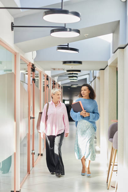 istock Two Female Colleagues Chatting while Walking along Corridor in Office Building 2190229552