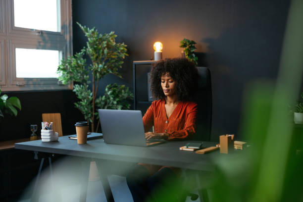 istock Focused young woman working on laptop in modern office surrounded by plants 2190232070
