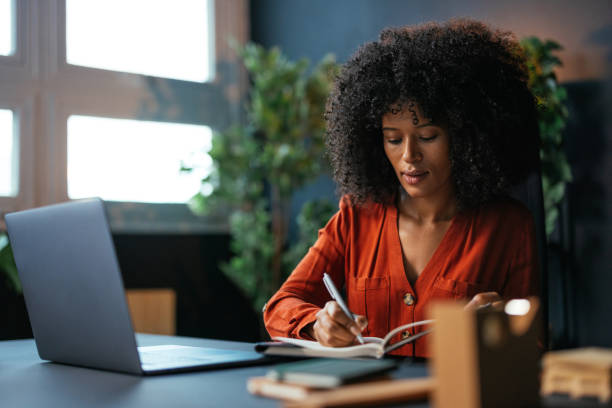 istock Focused young woman writing in notebook at home office desk 2190232080