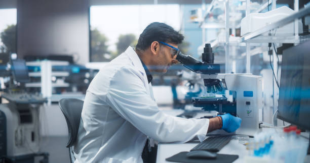 istock Molecular Biology Research Scientist Looking at a DNA Sample Under a Microscope in an Applied Science Laboratory. Portrait of an Adult Lab Engineer in White Coat Working on Vaccine and Medicine 2190233804