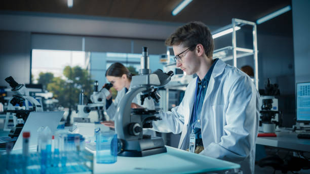 istock Portrait of a Young Smart Scientist Working in a Laboratory, Using Advanced Microscope, Writing Down Research Data in a Paper Notebook. Caucasian Biotechnology Specialist Using Modern Tools 2190240978