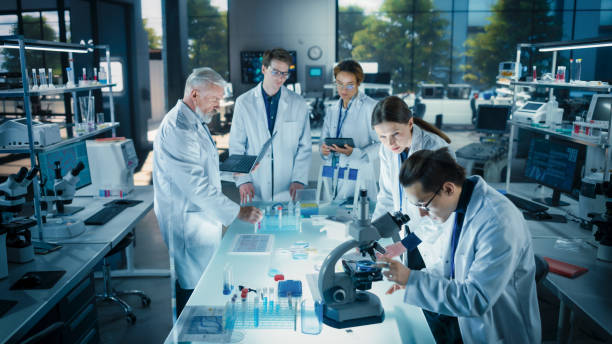 istock Head of Laboratory Making a Bioengineering Experiment with a Group of Young Science College Students. Future Specialists Working with Modern Microscopes, Using Tablet and Laptop Computers 2190241115