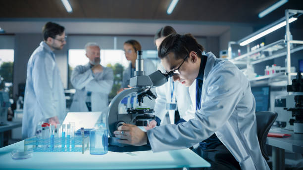istock Head of Laboratory Making a Bioengineering Experiment with a Group of Young Science College Students. Future Specialists Working with Modern Microscopes, Using Tablet and Laptop Computers 2190241206