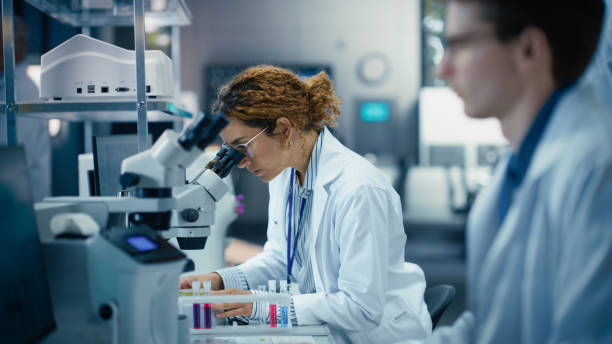 istock Medical Research and Development Laboratory: Beautiful Hispanic Female Scientist Working on a Computer and Looking at a Sample in a Petri Dish Under a Microscope. Advanced Biotechnology Lab 2190241625