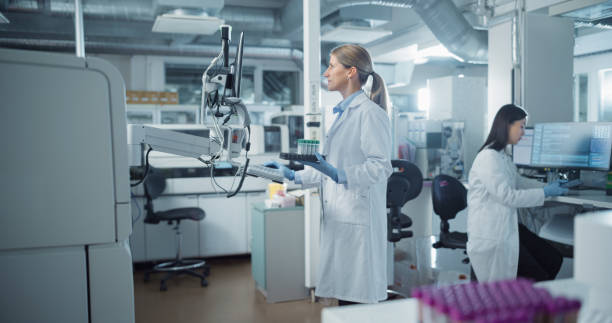 istock Scientist in White Lab Coat Operates Advanced Testing Equipment in Modern Laboratory. Handling Samples and Analyzing Data on a Computer. Researcher Working with Colleagues in a High-tech Environment 2190246605