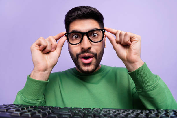 istock Photo of impressed excited handsome geek man dressed green pullover hands touch glasses staring isolated on violet color background 2190247087