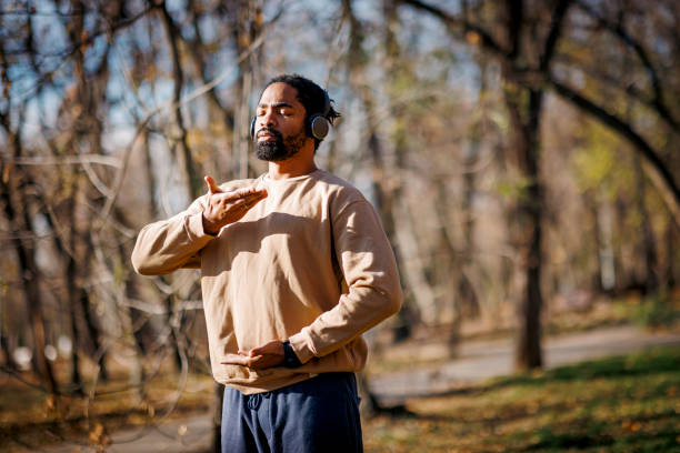 Young man practicing qigong in a public park wearing headphones