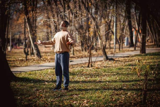 Young adult man wearing headphones is practicing mindfulness and deep breathing exercises in a peaceful park setting, embracing a healthy lifestyle