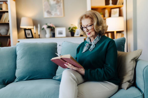 istock Senior woman reading book, sitting on sofa and resting at home 2190257280