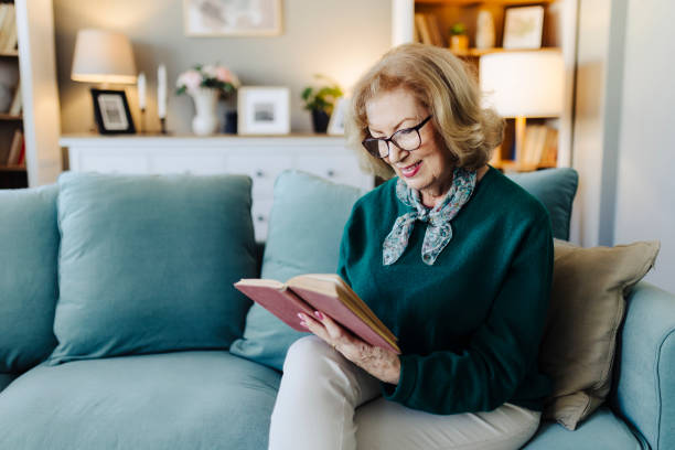istock Senior woman reading book, sitting on sofa and resting at home 2190257635