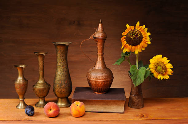 Still life, copper dishes, sunflower, book and fruit on a wooden table