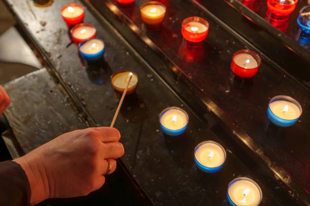 A close-up of a hand holding a matchstick to light a votive candle in a colorful arrangement placed on a wooden table, creating a peaceful and reflective mood.