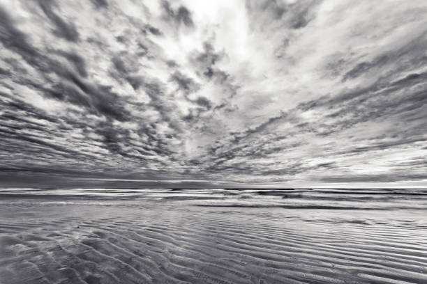 A portrait landscape in black and white of a reflective rocky beach in Denmark with impressive and contrasty clouds