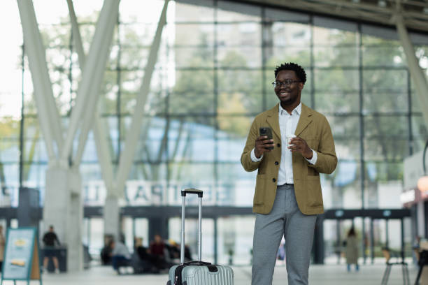 istock Young Professional at Airport with Suitcase and Coffee, Using Smartphone 2190267181