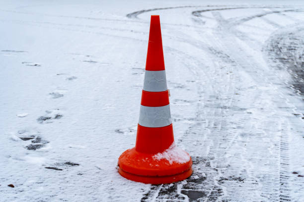 istock A bright orange traffic cone is placed on a snowy surface in a parking lot, showing tire tracks and footprints around it 2190271967