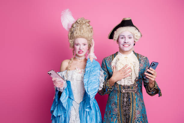 istock Two people dressed in elegant historical costumes against a pink background, holding smartphones and expressing surprise. 2190274487