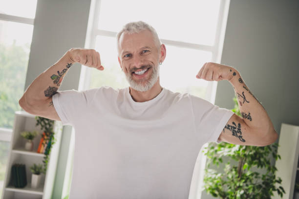 istock Elderly man with tattoos flexing muscles in white t-shirt in a bright indoor setting 2190274870