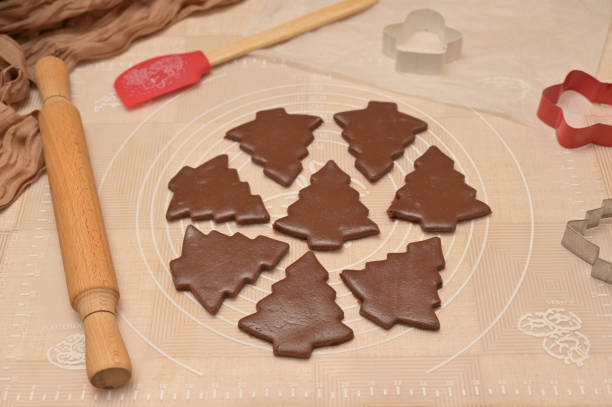 Christmas homemade baking, brown cocoa dough cut into tree shapes for baking gingerbread, cutter, rolling pin, spatula on the table