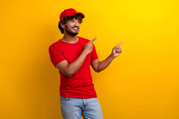 istock Smiling young man in red attire pointing on vibrant yellow background 2190277540