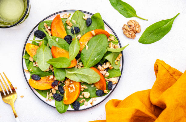 istock Wintervegan persimmon salad with walnuts, blue raisin and spinach, white background, top view 2190277702