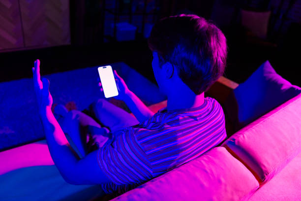 istock Young man relaxing on a couch lit with vivid neon lights holding a smartphone 2190279208