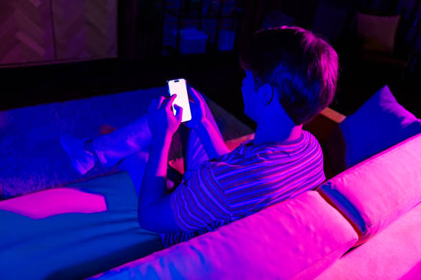 istock Young man using smartphone at home in vibrant colored lighting, relaxing on a sofa in a modern living room 2190279217