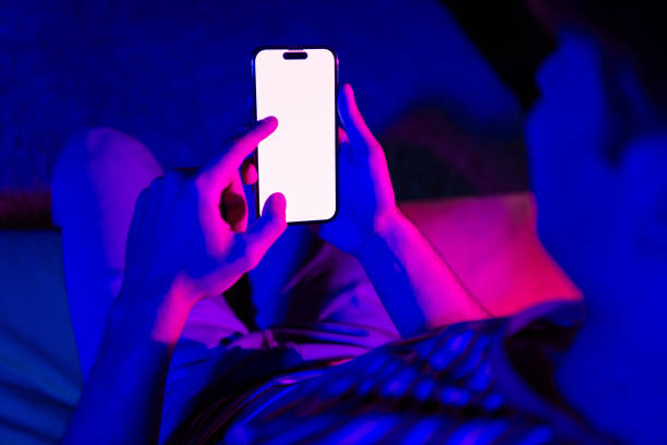 istock Young man using smartphone illuminated with vibrant colors in cozy home interior 2190279227