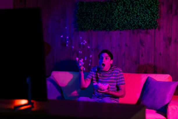 istock Young man enjoying leisure time indoors, watching television with popcorn during a vibrant evening, expressing shock and amazement 2190279257