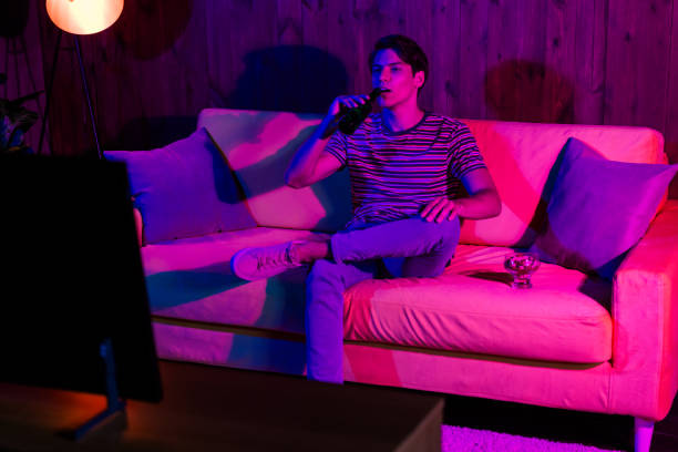 istock Young man relaxing on a couch while watching TV, illuminated by colorful ambient lighting 2190279287
