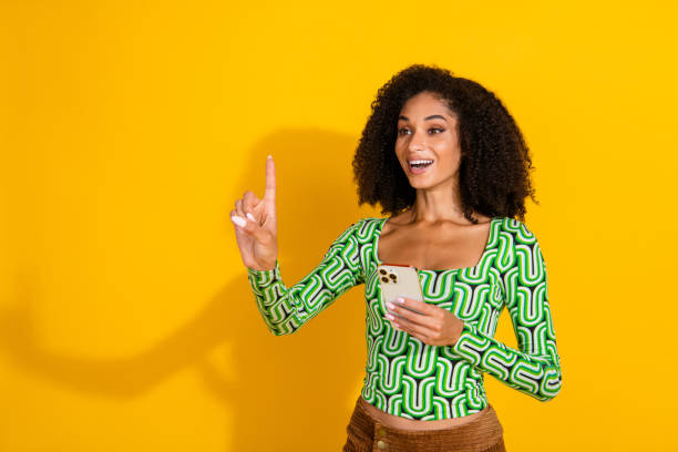 istock Young woman with a joyful expression holding a smartphone in front of a bright yellow background 2190279875