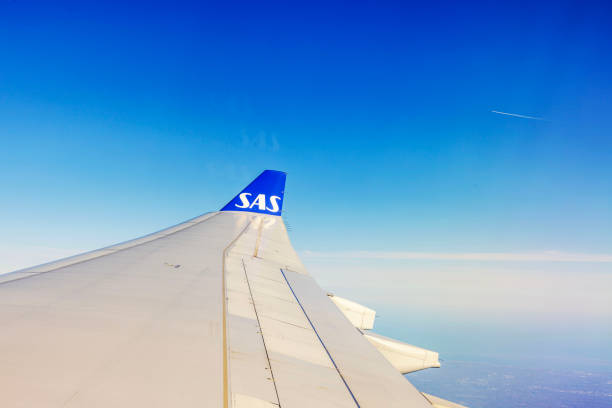 USA. New York. 12.17.2024. SAS airplane wing with logo visible during flight under clear blue sky at high altitude.