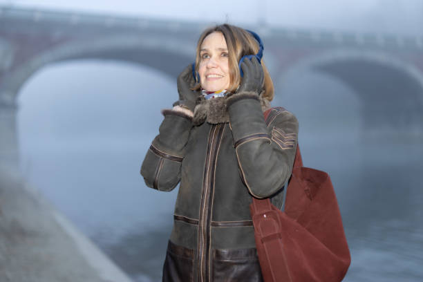 A beautiful woman listens to music with headphones walking along the river Po in a foggy winter afternoon.The music can take you to an inner world, where there is no cold, no dampness, but light and color.