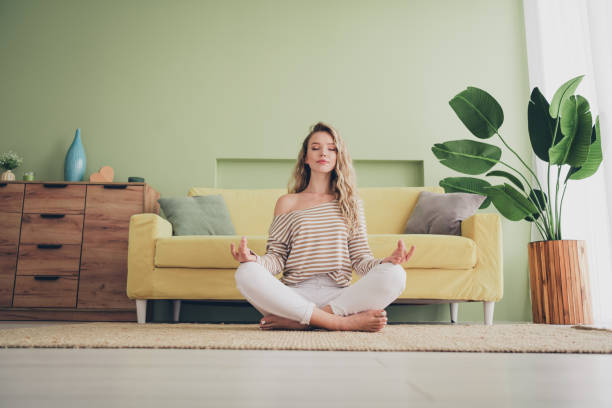 istock Relaxed young woman in casual striped pullover meditating at home on a sunny day, enjoying peaceful ambience in cozy living room with modern decor and indoor plant 2190283021