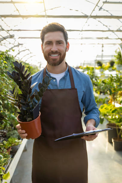 istock Young bearded man holding a potted flower and looking contented 2190284242