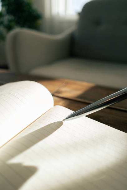 istock Silver pen touching blank page of notebook in sunlit room 2190286416
