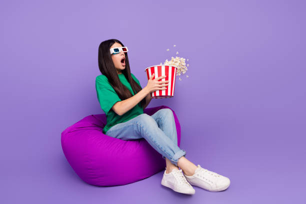 istock Young woman in 3D glasses enjoying popcorn on a bean bag with surprise expression 2190289171