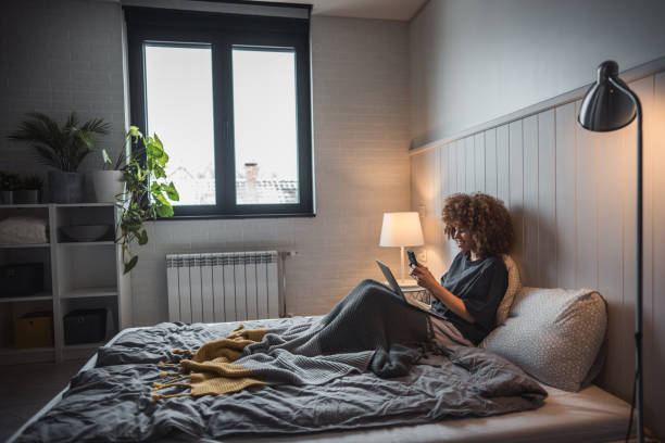 istock Efficient multitasking - Young woman with afro curls managing phone and laptop in bed 2190290587