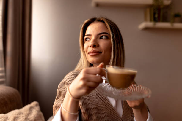 istock Smiling young woman drinking cappuccino at home on sofa 2190293802