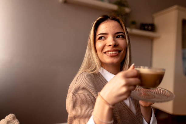 istock Smiling young woman drinking cappuccino at home on sofa 2190293804