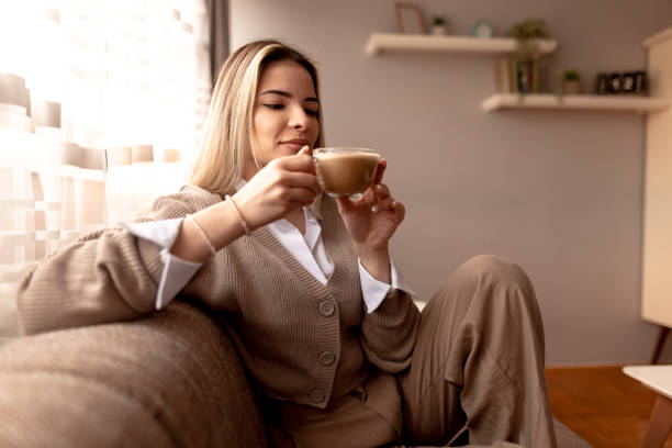 istock Smiling young woman drinking cappuccino at home on sofa 2190293819