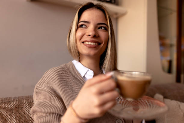istock Smiling young woman drinking cappuccino at home on sofa 2190293842