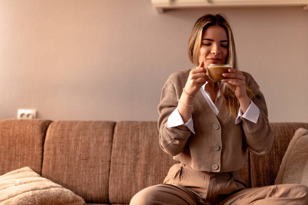 istock Smiling young woman drinking cappuccino at home on sofa 2190293856