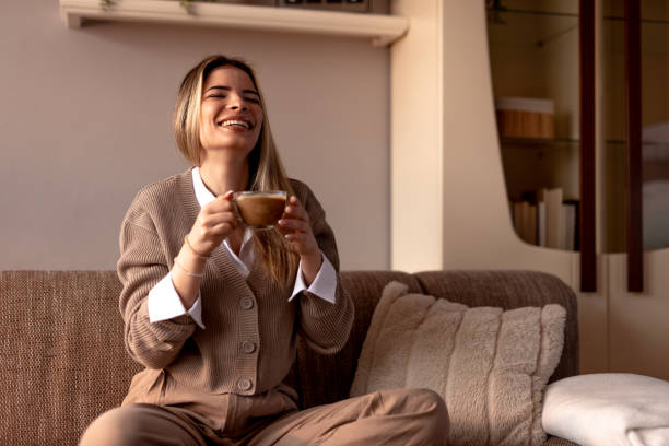 istock Smiling young woman drinking cappuccino at home on sofa 2190293857