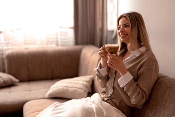 istock Smiling young woman drinking cappuccino at home on sofa 2190293871